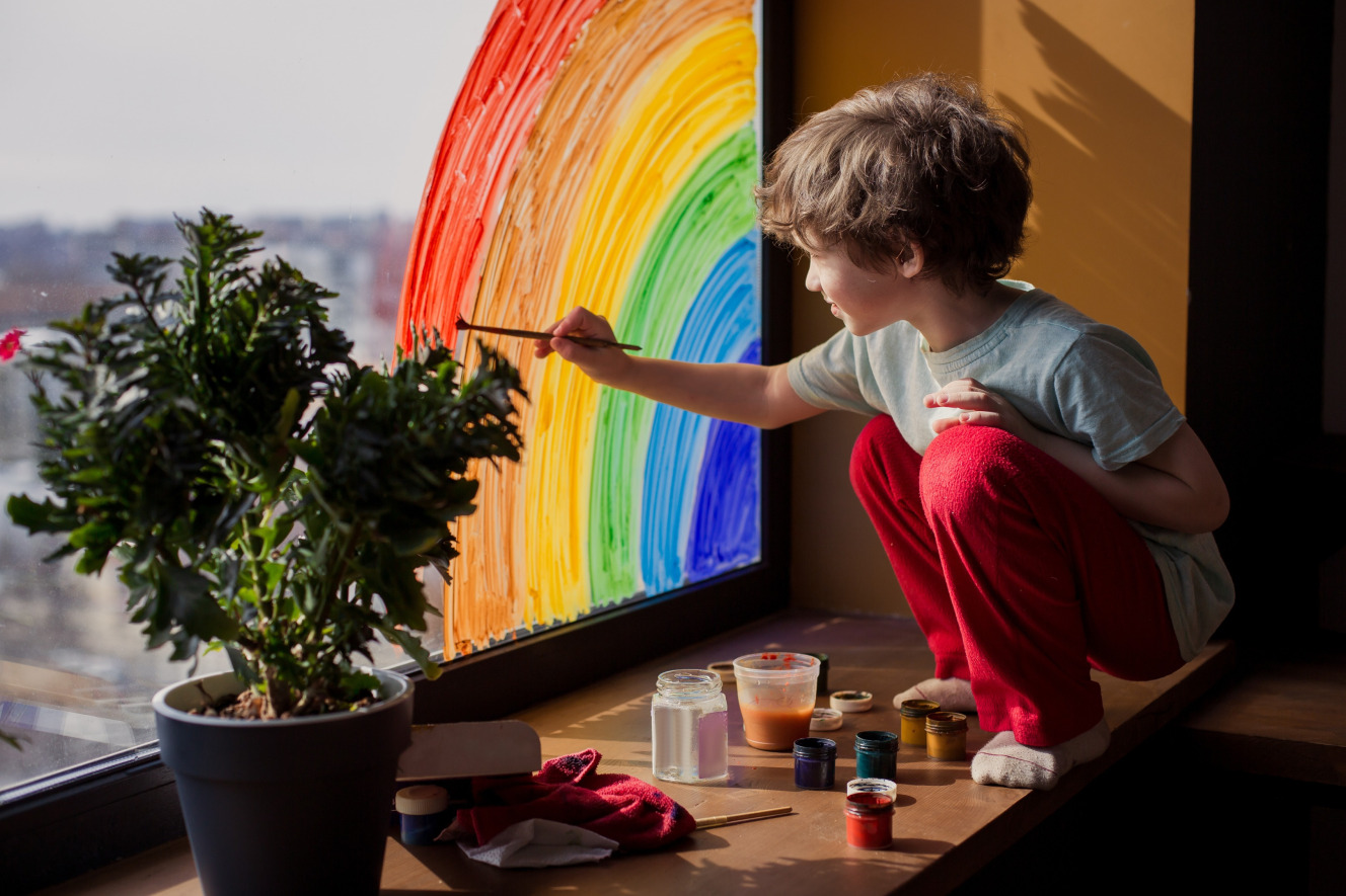 Child painting a rainbow on a window during a creative session guided by an ABA therapy specialist, fostering self-expression, fine motor skills, and sensory engagement.